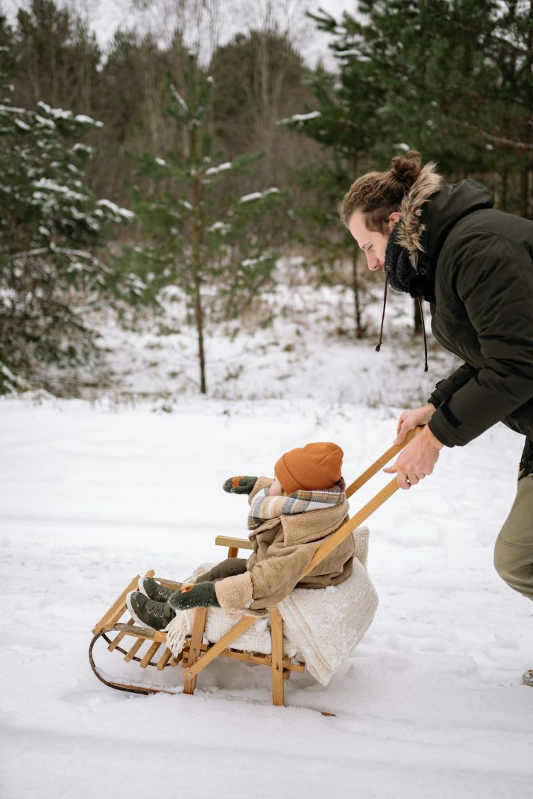 A man pushes a child on a sled in a snowy forest, enjoying outdoor winter recreation.