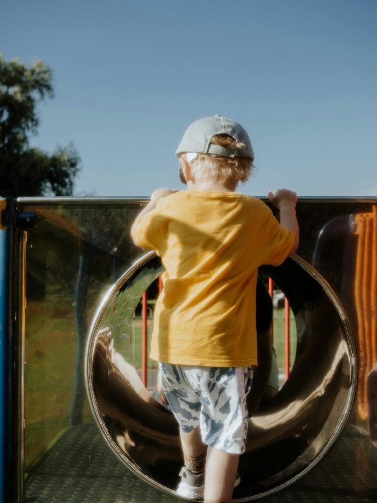 A young child climbing a playground slide on a sunny summer day, enjoying outdoor play.