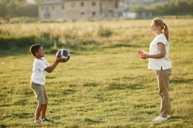 Mother and son enjoying a playful soccer game in a sunny meadow.